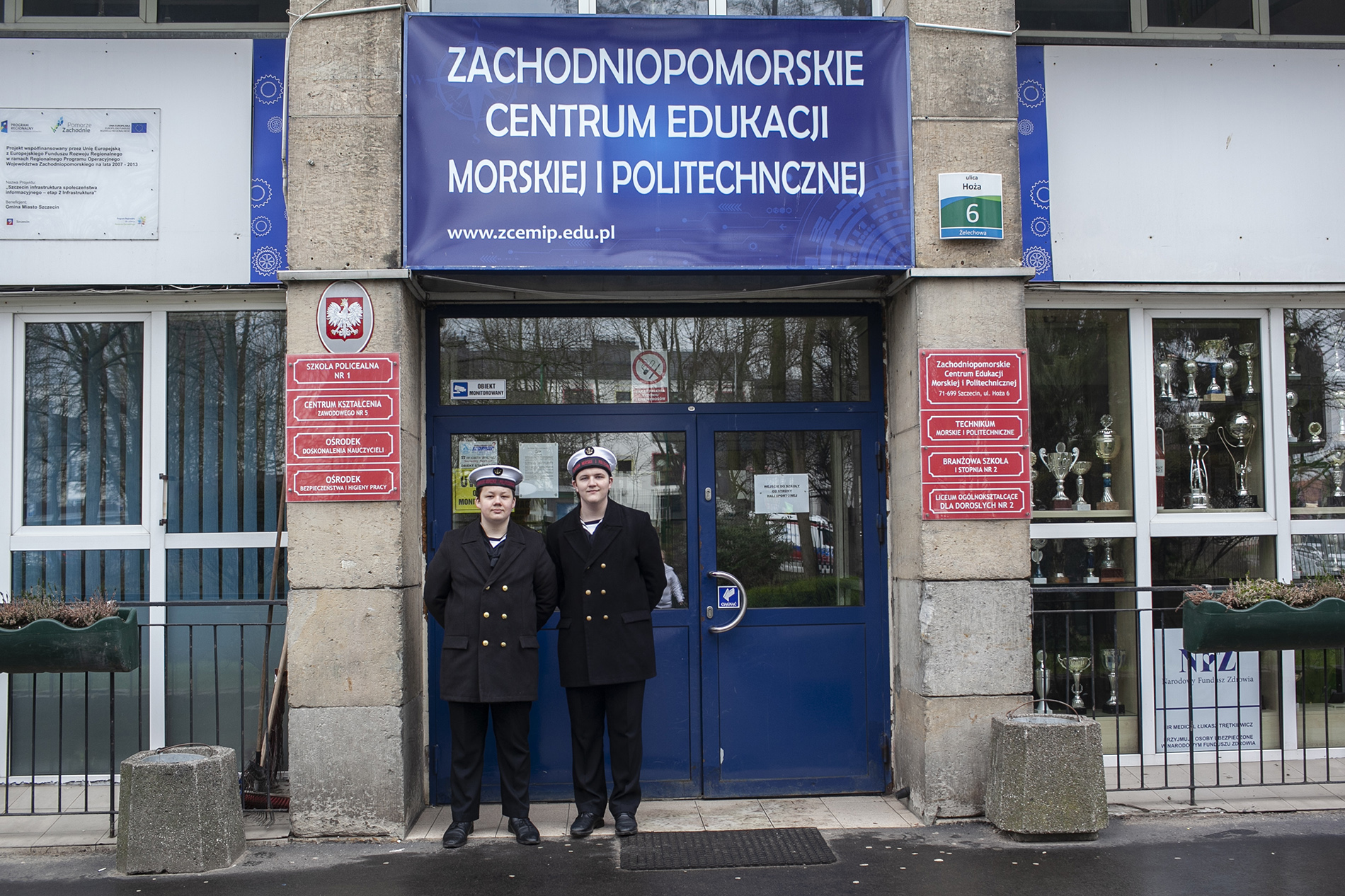 Dwóch uczniów w mundurach szkolnych przed wejściem do budynku ZCEMiP