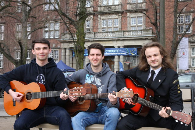 3 studentów Politechniki Morskiej w Szczecinie z gitarami na ławce przed budynkiem uczelni