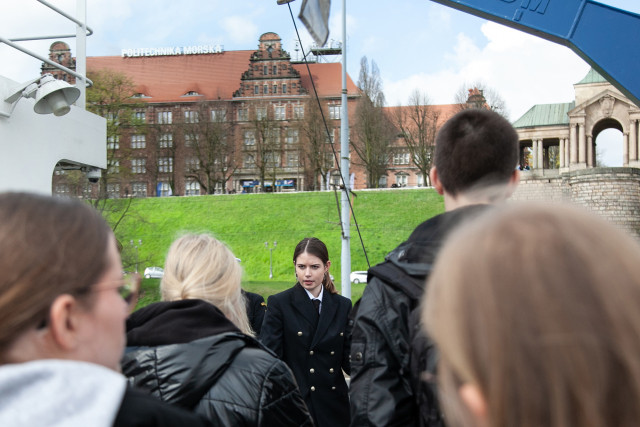  Studentka oprowadza uczniów po statku Nawigator XXI, w tle widok na budynek PM