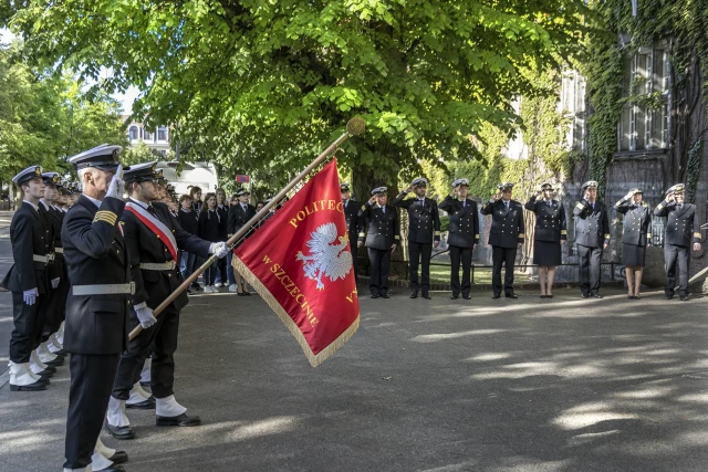 Kompania Honorowa PM z Pocztem Sztandarowym i dowódcą oraz pracownicy PM podczas uroczystości wciągnięcia bandery na maszt przy budynku uczelni z okazji Święta Szkoły 