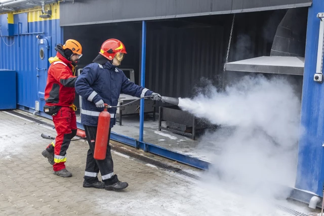 Student gasi pozorowany pożar  gaśnicą w asyście instruktora
