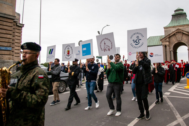 Przedstawiciel szczecińskich uczelni z tablicami z logami uczelni podczas marszu Spacerek na Uniwerek