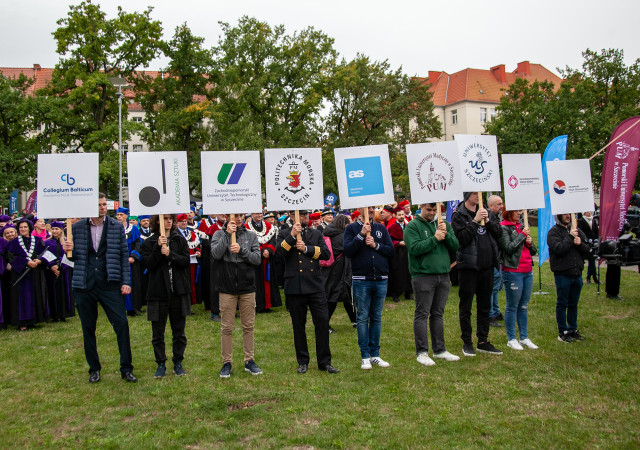 Przedstawiciel szczecińskich uczelni z tablicami z logami uczelni po marszu Spacerek na Uniwerek