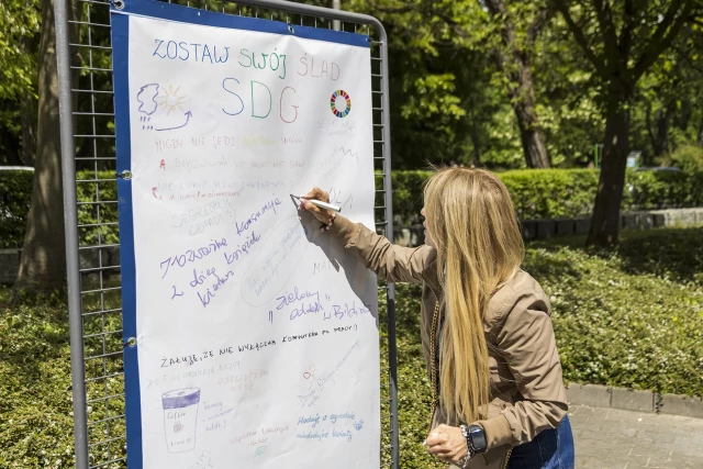 Pracowniczka PM pisze hasło na banerze "Zostaw swój ślad SDG"