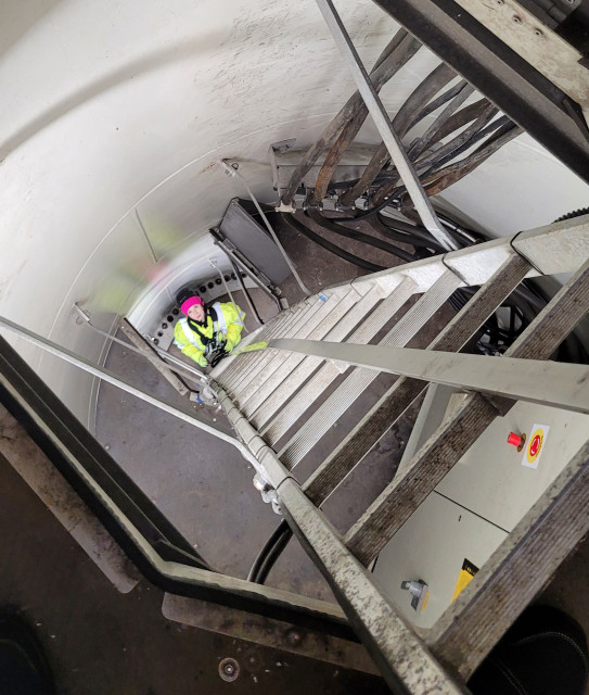 Student wchodzi po drabinie wewnątrz masztu szkoleniowej turbiny wiatrowej PM