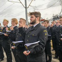 Mundurowi studenci I roku PM, na tle statku Nawigator XXI, trzymając czapki na dłoni ślubują podczas uroczystości inauguracji nowego roku akademickiego 2023/24