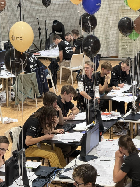 Studenci w trakcie właściwego konkursu, rozwiązujący zadania algorytmiczne wraz z wiszącymi balonikami za każde poprawne rozwiązanie 