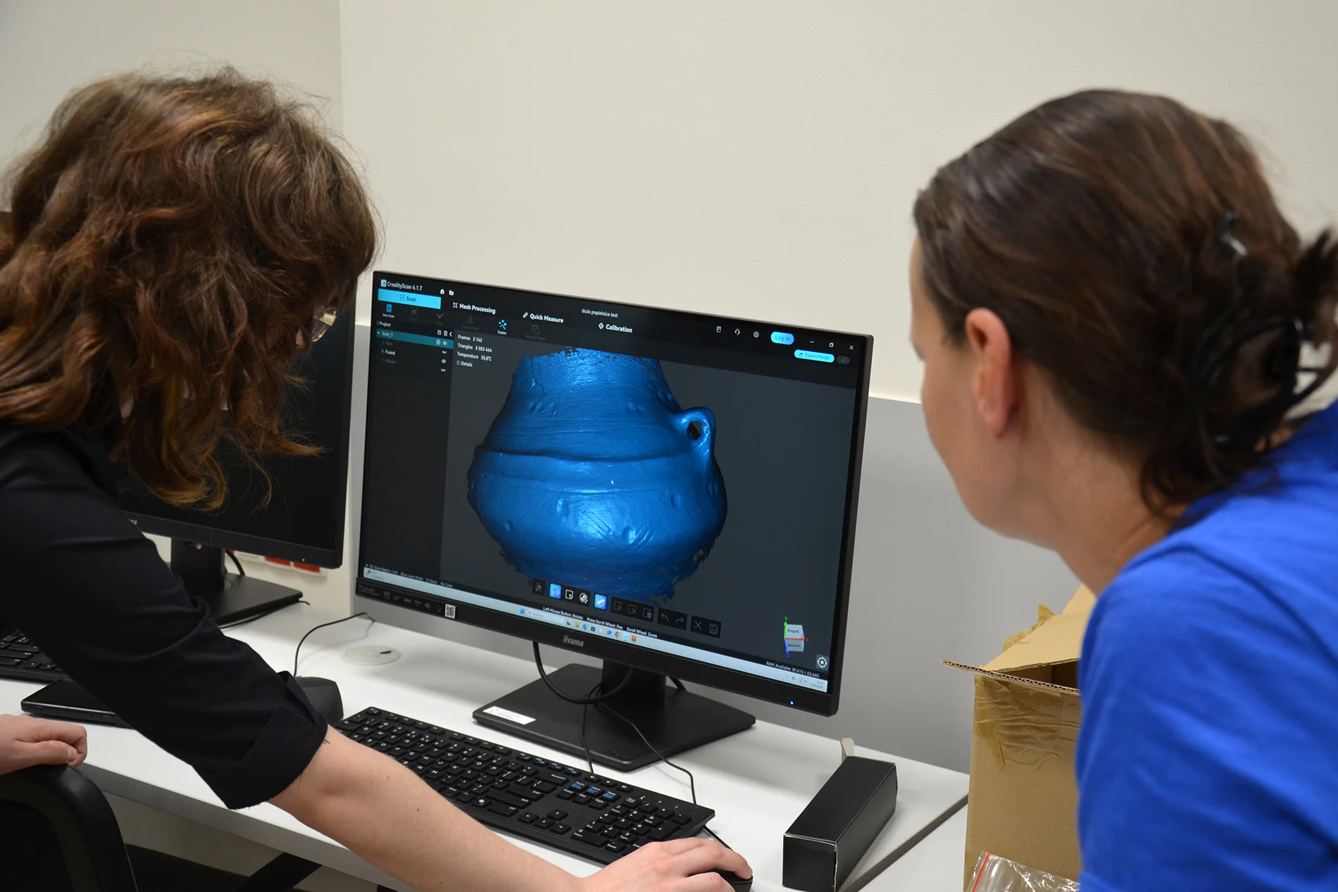 Dwie osoby patrzą na skan 3D naczynia pradziejowego na ekranie komputera
