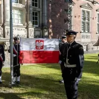 Studenci z Kompanii Honorowej PM wciągają na maszt banderę przed budynkien uczelni z okazji Święta Szkoły
