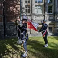 Studenci z Kompanii Honorowej PM wciągają na maszt banderę przed budynkiem uczelni w dniu Święta Szkoły