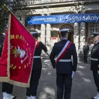 Kompania Honorowa PM z pocztem sztandarowym i dowódcą oraz pracownicy PM podczas uroczystości  wciągnięcia bandery przy budynku uczelni z okazji Święta Szkoły 
