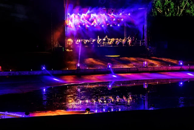 Widok widowni i rozświetlonej sceny z artystami po zmierzchu