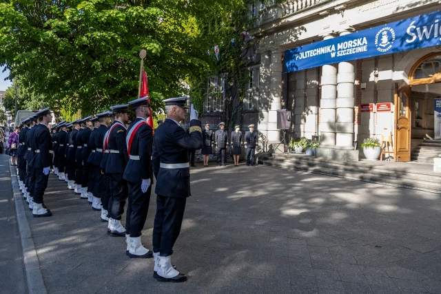 Kompania Honorowa PM z pocztem sztandarowym i dowódcą oraz pracownicy PM podczas uroczystości podniesienia bandery przy budynku uczelni z okazji Święta Szkoły 