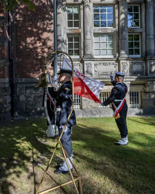Studenci z Kompanii Honorowej PM wciągają na maszt banderę przed budynkiem uczelni w dniu Święta Szkoły