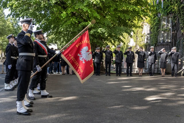 Kompania Honorowa PM z pocztem sztandarowym i dowódcą oraz pracownicy PM podczas uroczystości wciągnięcia bandery przy budynku uczelni z okazji Święta Szkoły 