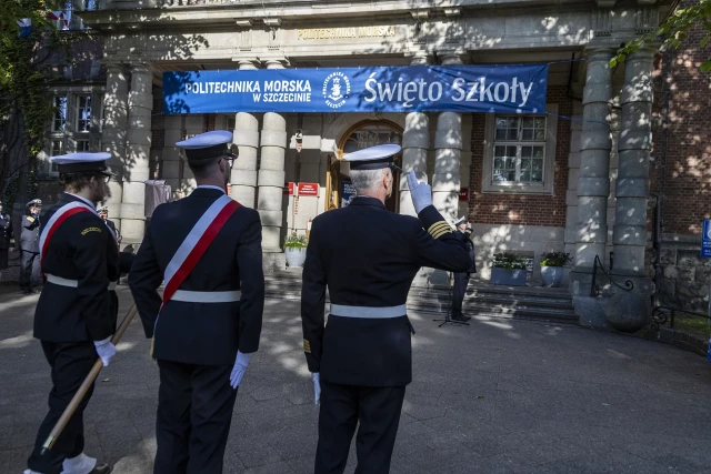 Kompania Honorowa PM z pocztem sztandarowym i dowódcą oraz pracownicy PM podczas uroczystości  wciągnięcia bandery przy budynku uczelni z okazji Święta Szkoły 